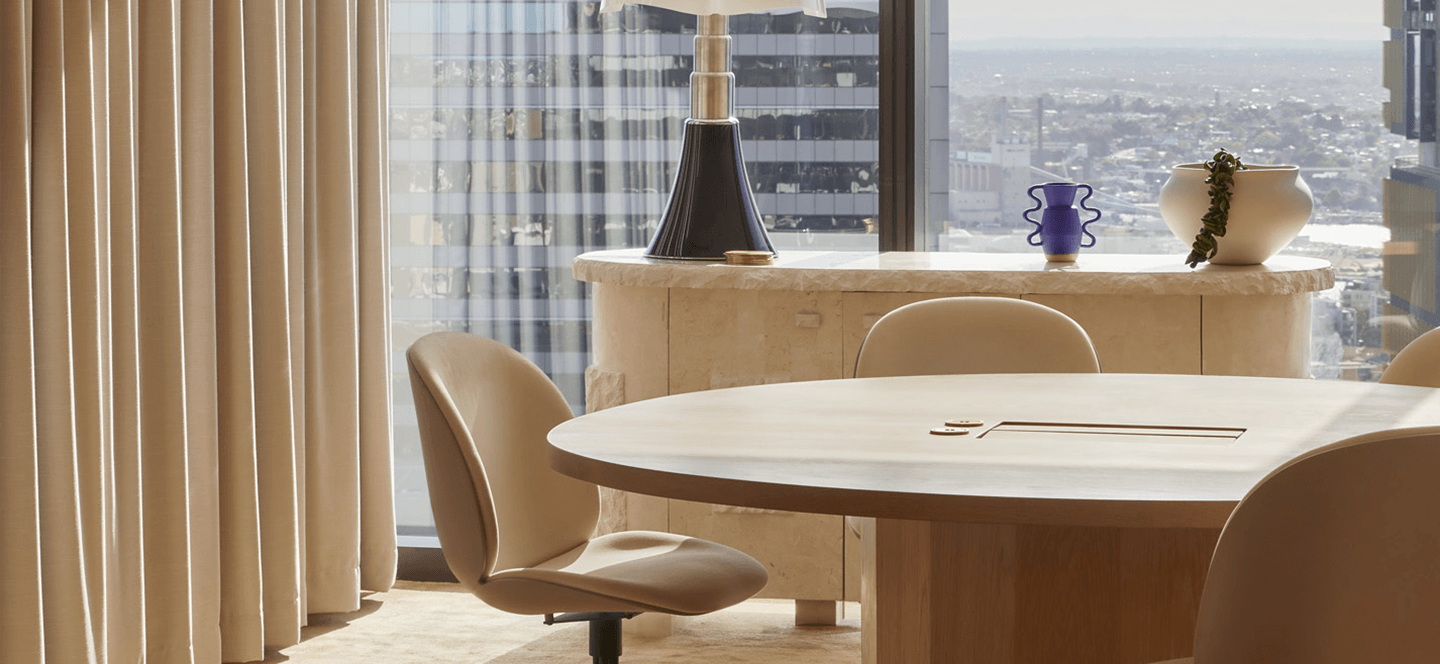 Office meeting room with chairs around table, floor to ceiling windows with building visible.